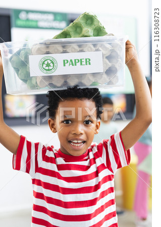 Young African American boy holds recycle bin above his head in classroom at school Young African American boy holds recycle bin above his head in classroom at school 116308723
