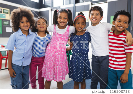 In school, six young students are standing together in classroom, smiling 116308738