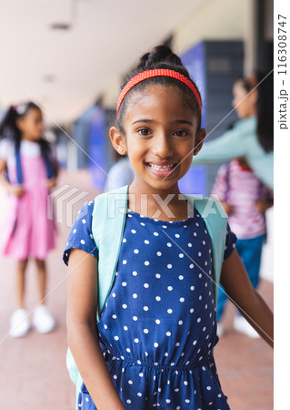 Young biracial girl wearing polka-dot dress and backpack is smiling outdoors Young biracial girl wearing polka-dot dress and backpack is smiling outdoors 116308747