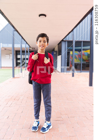 In school, young biracial male student wearing a red sweater is standing outside 116308759