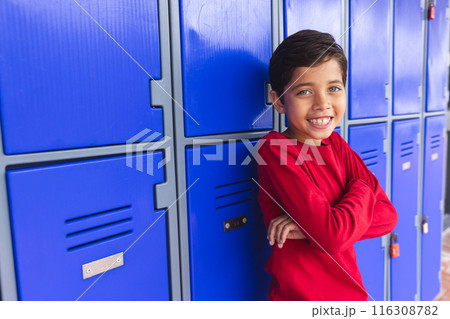 Biracial boy stands by blue lockers outdoors, arms crossed, with copy space 116308782