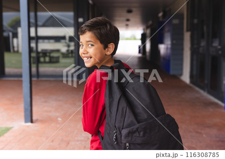 In school, young biracial male student wearing a red shirt is walking outdoors 116308785