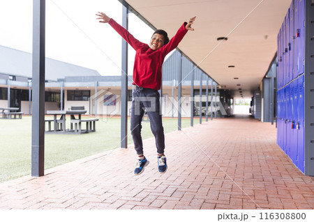 In school, outdoors, a biracial young boy is jumping with joy 116308800