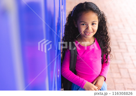 In school, outdoors, young biracial girl leaning against a locker, wearing a pink top 116308826