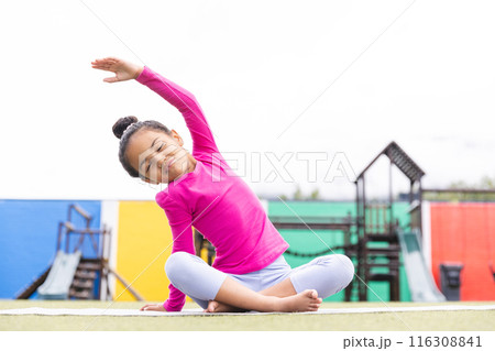 In school, young biracial girl stretching on a mat outdoors doing yoga 116308841