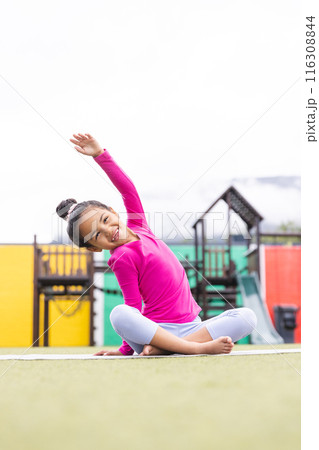 In school, young biracial girl in pink and gray stretches on playground doing yoga 116308844