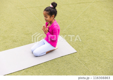 In school, young biracial girl wearing pink is practicing yoga outdoors 116308863