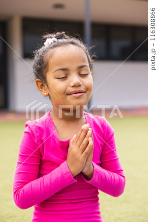 In school, young biracial girl with closed eyes is standing outside doing yoga In school, young biracial girl with closed eyes is standing outside doing yoga 116308866