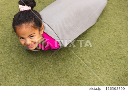 In school, outdoors, a biracial young girl wearing pink is lying on her stomach 116308890