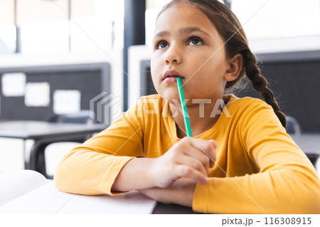 In school, in classroom, young biracial girl holding a pencil, looking thoughtful 116308915