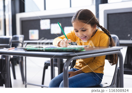 In school, young biracial girl with brown hair wearing a yellow top is writing in the classroom In school, young biracial girl with brown hair wearing a yellow top is writing in the classroom 116308924