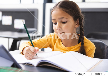 In school, young biracial girl with braided hair focusing on writing in the classroom 116308937