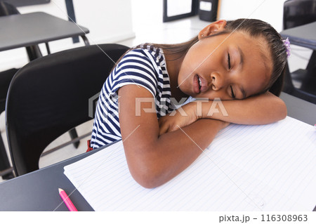 In school, young biracial girl with light brown skin is sleeping at her desk in the classroom In school, young biracial girl with light brown skin is sleeping at her desk in the classroom 116308963