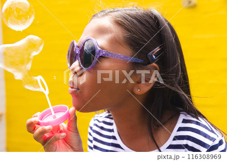In school, young biracial girl wearing sunglasses is blowing bubbles outdoors In school, young biracial girl wearing sunglasses is blowing bubbles outdoors 116308969