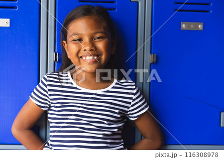 In school, young biracial female student leaning against blue lockers, smiling outdoors In school, young biracial female student leaning against blue lockers, smiling outdoors 116308978