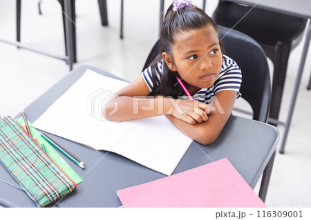 In school, young biracial girl sitting at a desk in a classroom, looking thoughtful In school, young biracial girl sitting at a desk in a classroom, looking thoughtful 116309001