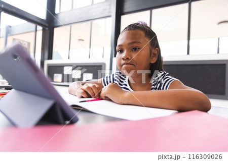 In school, young biracial girl with light brown skin focusing on a tablet in the classroom In school, young biracial girl with light brown skin focusing on a tablet in the classroom 116309026