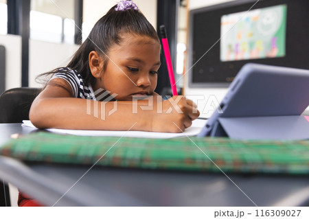 In school, young biracial girl focusing on writing in her notebook in the classroom In school, young biracial girl focusing on writing in her notebook in the classroom 116309027