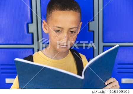 In a school, a young biracial boy stands before a blue locker background 116309103