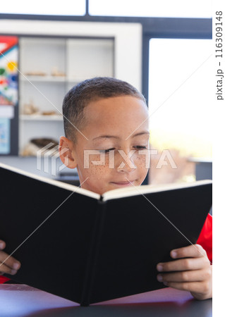 Biracial boy engrossed in reading a book at school 116309148