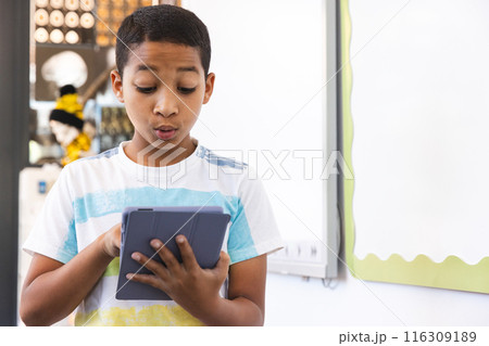 Biracial boy looks surprised at a tablet in a bright room at school Biracial boy looks surprised at a tablet in a bright room at school 116309189