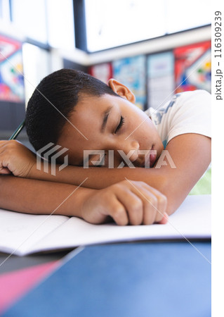 Biracial boy asleep on his desk in the classroom at school 116309239