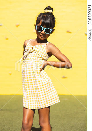Biracial girl wearing sunglasses and a sundress poses confidently outdoors 116309321