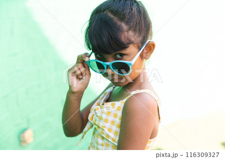 Biracial girl wearing sunglasses and a sundress poses playfully outdoors Biracial girl wearing sunglasses and a sundress poses playfully outdoors 116309327