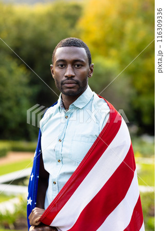 Portrait of serious african american man covered with flag of usa in garden 116309336