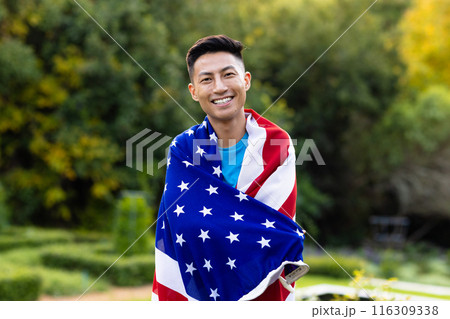 Portrait of happy asian man covered with flag of usa in garden 116309338