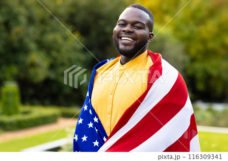Portrait of happy african american man covered with flag of usa in garden 116309341