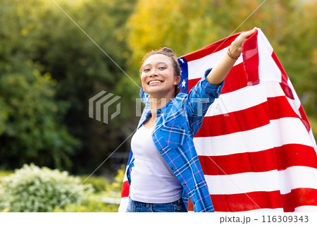 Portrait of happy asian woman covered with flag of usa in garden 116309343