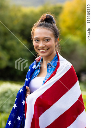 Portrait of happy asian woman covered with flag of usa in garden 116309350