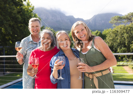 Diverse senior female friends holding drinks, enjoying outdoors 116309477