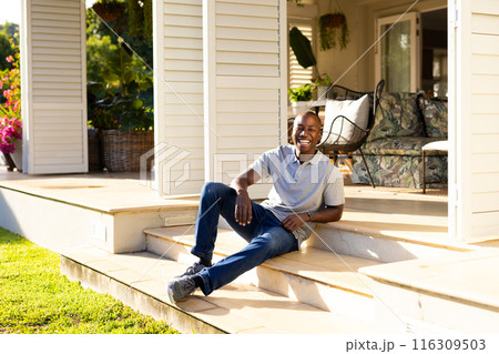 Outdoors, young African American man sitting on steps smiling at camera on sunny day Outdoors, young African American man sitting on steps smiling at camera on sunny day 116309503