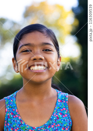 Outdoors, young biracial girl smiling brightly, wearing colorful floral dress 116309539