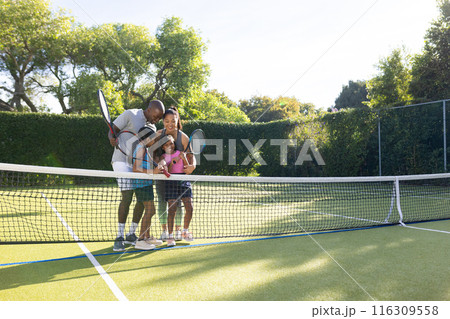Outdoors, diverse family of four enjoying game of tennis together on outdoor court Outdoors, diverse family of four enjoying game of tennis together on outdoor court 116309558
