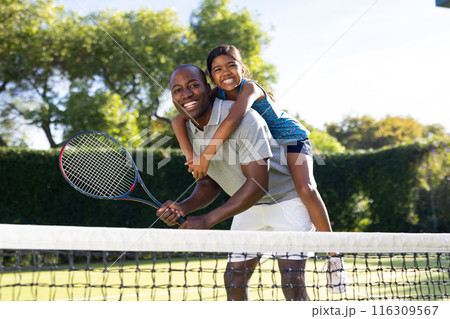 Outdoors, diverse father and daughter on tennis court with lush green trees 116309567