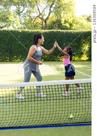 Outdoors, biracial mother and daughter giving high-five on tennis court 116309584