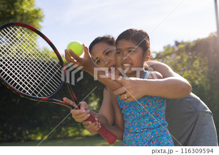 Outdoors biracial mother and daughter teaching tennis, focused on holding racket 116309594