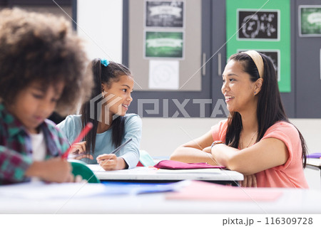 Biracial female teacher interacting with two students in classroom Biracial female teacher interacting with two students in classroom 116309728