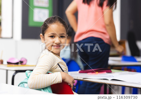 Biracial girl sitting at desk in classroom, smiling at camera Biracial girl sitting at desk in classroom, smiling at camera 116309730