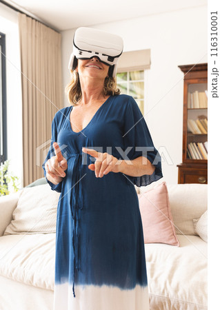 Senior caucasian woman using virtual reality headset, at home 116310001