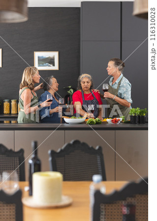 Diverse group of mature women enjoying wine and preparing food together in kitchen Diverse group of mature women enjoying wine and preparing food together in kitchen 116310028