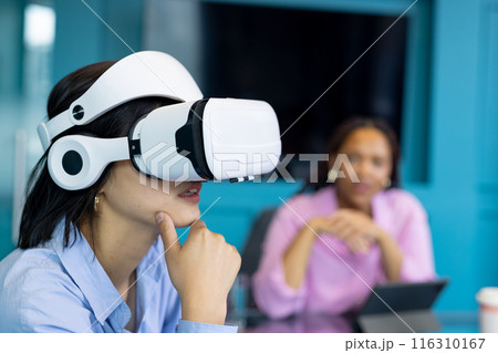 Asian young woman uses VR headset as biracial young woman observes, collaborating on business 116310167