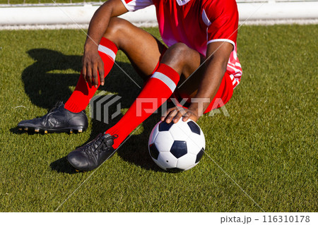African American soccer player sitting on grass holding soccer ball African American soccer player sitting on grass holding soccer ball 116310178