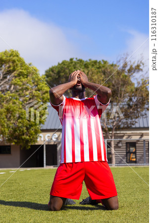African American soccer player kneeling on grass, appearing emotional 116310187