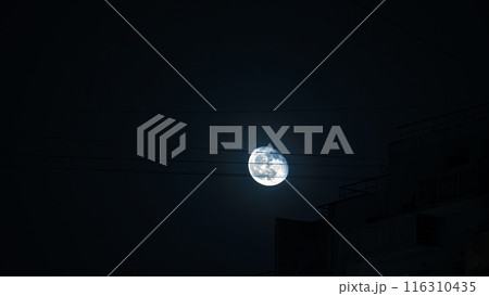 Night city scene with full bright moon against dark blue sky and electric wires. The atmosphere is mysterious and serene. Night city scene with full bright moon against dark blue sky and electric wires. The atmosphere is mysterious and serene. 116310435