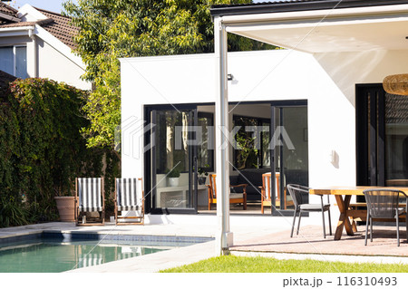 Modern backyard with pool, lounge chairs, and outdoor dining area in sunny weather, copy space 116310493