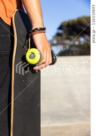 Holding skateboard, male student enjoying sunny day while standing outdoors Holding skateboard, male student enjoying sunny day while standing outdoors 116310693